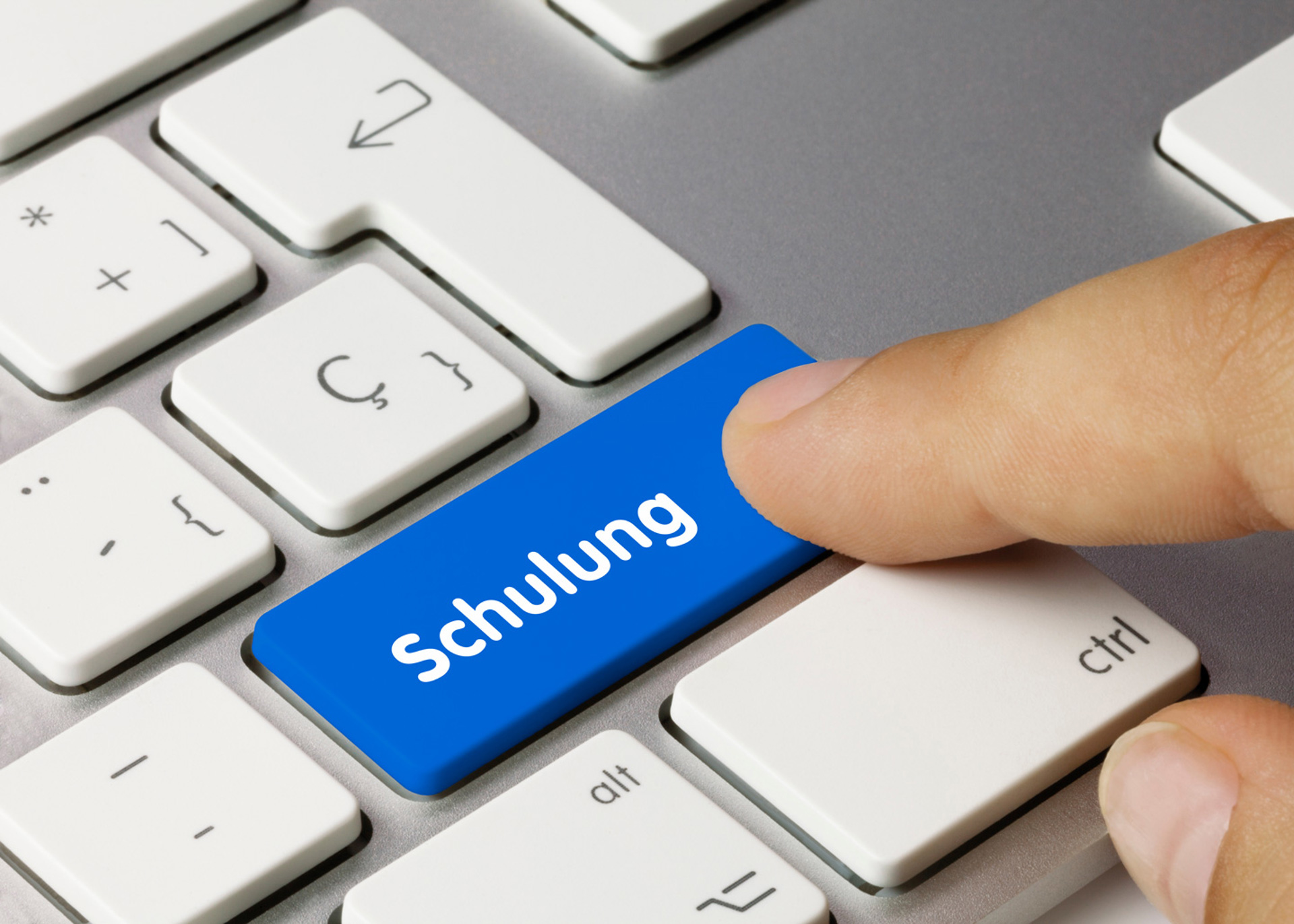 Finger drückt blaue Taste mit dem Wort 'Schulung' auf einer Computertastatur